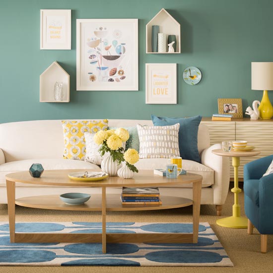 Teal blue living room, cream sofa with cushions, wooden coffee table, wall mounted prints.