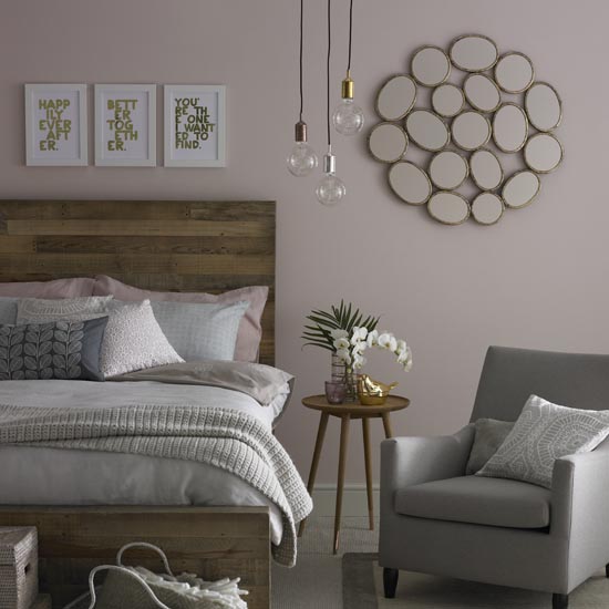Pink bedroom, natural wooden bedframe. framed pictures, pendant lighting, wood bedside table, grey armchair. Pub Orig